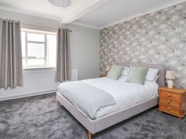 A bedroom with a bed featuring pillows and a throw blanket beside wooden nightstands with lamps at Bewholme in Skipsea