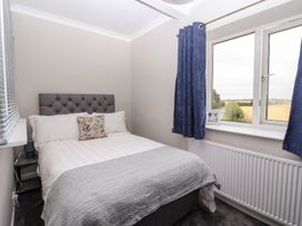 A bedroom with a double bed and gray headboard next to a window with blue curtains at Bewholme in Skipsea