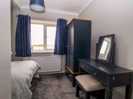 A bedroom with a bed, blue curtains, a wardrobe, a dressing table with a mirror, and a stool at Bewholme in Skipsea