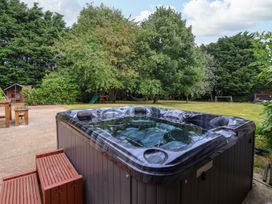 An outdoor hot tub with steps next to a lawn with trees and a children's play structure at Bewholme in Skipsea