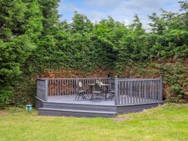 An outdoor wooden deck with a table and chairs surrounded by tall hedges at Bewholme in Skipsea
