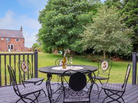 A patio with black metal table and chairs overlooking a garden with trees and a brick house in the background at Bewholme in Skipsea