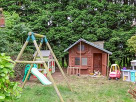 A backyard play area with a wooden swing set slide playhouse toy car and toy vehicles at Bewholme in Skipsea