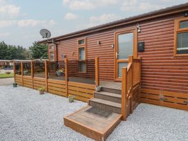 An exterior view of a wooden cabin with steps leading to a door surrounded by gravel and small potted plants at Lodge 2 in Auchterarder