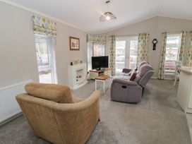 A living room with sofas a TV on a stand a small table a fireplace and windows with patterned curtains at Lodge 2 in Auchterarder