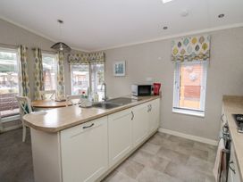 A kitchen with a sink and microwave next to a dining area with a round table and chairs at Lodge 2 in Auchterarder