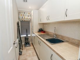 A narrow utility room with white cabinets a countertop with a sink cleaning tools and a window with patterned blind at Lodge 2 in Auchterarder