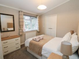 A bedroom with a double bed bedside lamps a chest of drawers and a window with curtains at Lodge 2 in Auchterarder