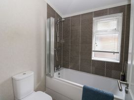 A bathroom with a bathtub shower combination, brown tiled wall, toilet, window with blinds, and blue towel on the bathtub at Lodge 2 in Auchterarder