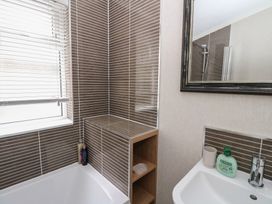 A bathroom with a bathtub, a sink with soap and a cup, a mirror, and tiled walls at Lodge 2 in Auchterarder