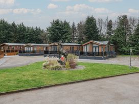 A driveway with a grass area and a stag statue in front of wooden lodges surrounded by trees at Lodge 2 in Auchterarder