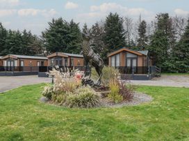 A garden with a stag statue and plants in front of wooden lodges surrounded by trees at Lodge 2 in Auchterarder
