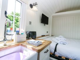 A small kitchen area with a sink toaster and cloths next to a bed with towels and a wall mounted tv at Airlie Burnside near Forfar