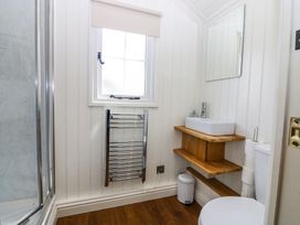 A bathroom with a shower, window, heated towel rail, sink, mirror, toilet, and wooden floor at Airlie Burnside near Forfar