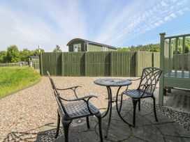 An outdoor patio with a metal table and two chairs on a circular stone platform surrounded by gravel and a green wooden fence at Airlie Burnside near Forfar