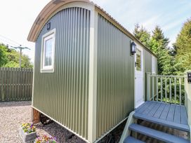 An exterior view of a small green corrugated metal cabin with a white door and window a small porch with blue stairs and railing and flowers in pots at the base of the cabin at Airlie in Burnside near Forfar
