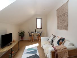 A small living room with a white sofa with patterned cushions a wooden table with a black TV a plant a dining table set for two and a wall hanging at Priory Barn Apartment in Walton near Street