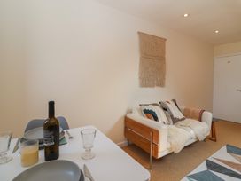 A small dining table with plates glasses and a bottle next to a couch with cushions and a wall hanging in Priory Barn Apartment Walton near Street
