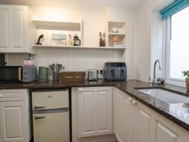 A kitchen with white cabinets a brown countertop a small refrigerator microwave kettle toaster and sink at Priory Barn Apartment Walton near Street