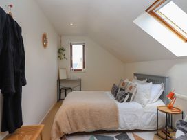 A bedroom with a bed multiple pillows a side table with a lamp a small desk and chair a window and a skylight at Priory Barn Apartment Walton near Street