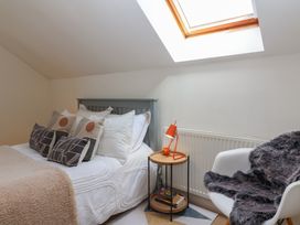 A bedroom with a bed multiple pillows a small side table with an orange lamp and a white chair with a fur throw at Priory Barn Apartment in Walton near Street