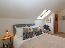 A bedroom with a bed with multiple pillows bedside tables with lamps a chair with a throw a skylight window and framed artwork at Priory Barn Apartment Walton near Street