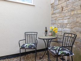 An outdoor seating area with two metal chairs with cushions a round table with a bottle of wine glasses and a vase of flowers at Priory Barn Apartment in Walton near Street
