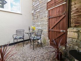 A small outdoor seating area with two metal chairs a round table with flowers and a bottle on gravel outside a stone wall and wooden door at Priory Barn Apartment in Walton near Street