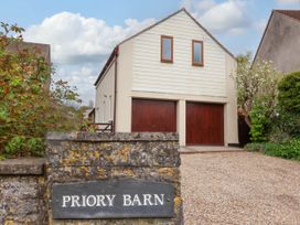 A building with two wooden garage doors and two small windows above a stone wall with a Priory Barn sign at Priory Barn Apartment in Walton near Street