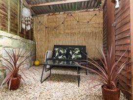 A small outdoor seating area with a black loveseat, glass coffee table, two potted plants, and string lights at Priory Barn Apartment Walton near Street