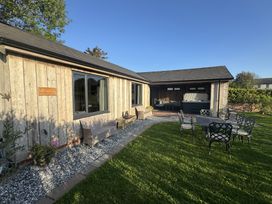 An outdoor wooden lodge with patio chairs a table a bench and a hot tub at Wayside Lodge in Blackpool