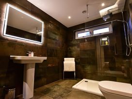 A bathroom with a lit mirror above a pedestal sink a shower area with a glass partition a towel rack with towels and a window at Wayside Lodge in Blackpool