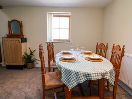 A dining room with a table set with plates and wine glasses six wooden chairs a cabinet a window and a plant at Walnut Cottage in Halkyn