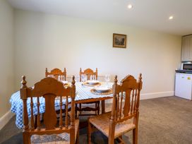 A dining area with a wooden table covered by a blue and white checkered tablecloth and four wooden chairs at Walnut Cottage in Halkyn