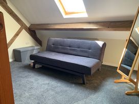 A room with a gray sofa bed a gray storage bench a wooden framed mirror and exposed wooden beams at Walnut Cottage in Halkyn