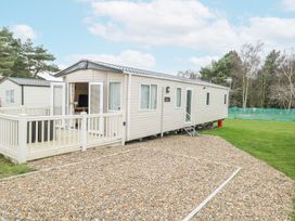 A mobile home with a small fenced deck and gravel driveway surrounded by grass and trees at 75 Foxburrow Hang in Fritton