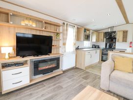 An open living area with a television above a fireplace lamp on a cabinet kitchen with cabinets and appliances and a sofa with a yellow cushion at 75 Foxburrow Hang in Fritton