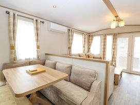 A seating area with a wooden dining table and cushioned benches next to windows with plaid curtains at 75 Foxburrow Hang in Fritton