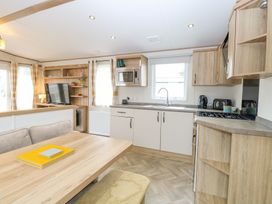 A kitchen and dining area with wooden cabinets a dining table and a television in a living space at 75 Foxburrow Hang in Fritton