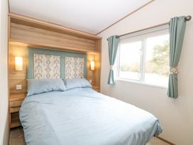A bedroom with a bed blue bedding bedside tables and a window with blue curtains at 75 Foxburrow Hang in Fritton