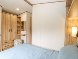 A bedroom with a bed with blue bedding wooden wardrobe and shelves with a lamp on the wall at 75 Foxburrow Hang in Fritton