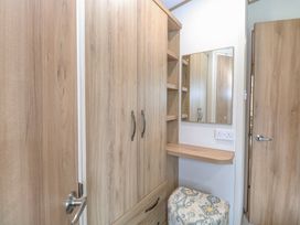 A wooden wardrobe with a mirror above a small shelf and a patterned ottoman in a room at 75 Foxburrow Hang in Fritton