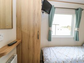 A bedroom with a bed near a window with curtains a wooden wardrobe and a small wall-mounted television at 75 Foxburrow Hang in Fritton