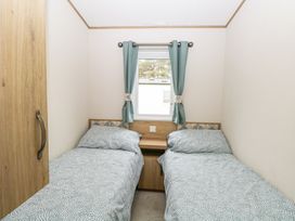 A bedroom with two single beds a window with curtains and a wooden cabinet at 75 Foxburrow Hang in Fritton