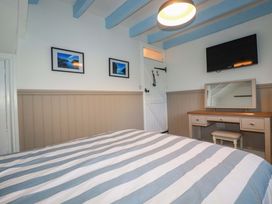 A bedroom with a bed, desk, mirror, tv, and pictures at Puffin Cottage in Tintagel
