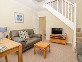 A living room with a grey sofa a wooden coffee table a TV on a wooden stand and a staircase at Malting Cottage in Dawlish