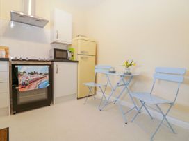 A kitchen with a stove microwave yellow refrigerator and a small table with two blue chairs and a flower vase at Malting Cottage in Dawlish