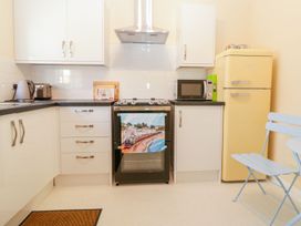 A kitchen with white cabinets a black stove a yellow refrigerator and a light blue folding chair at Malting Cottage in Dawlish
