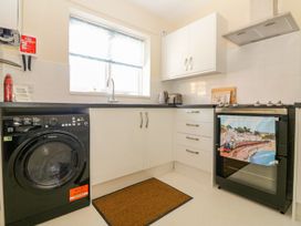 A kitchen with a washing machine, oven with a towel, countertop with kettle and toaster, and a window with a blind at Malting Cottage in Dawlish