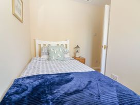 A single bed with patterned bedding and a blue blanket in a small bedroom at Malting Cottage in Dawlish